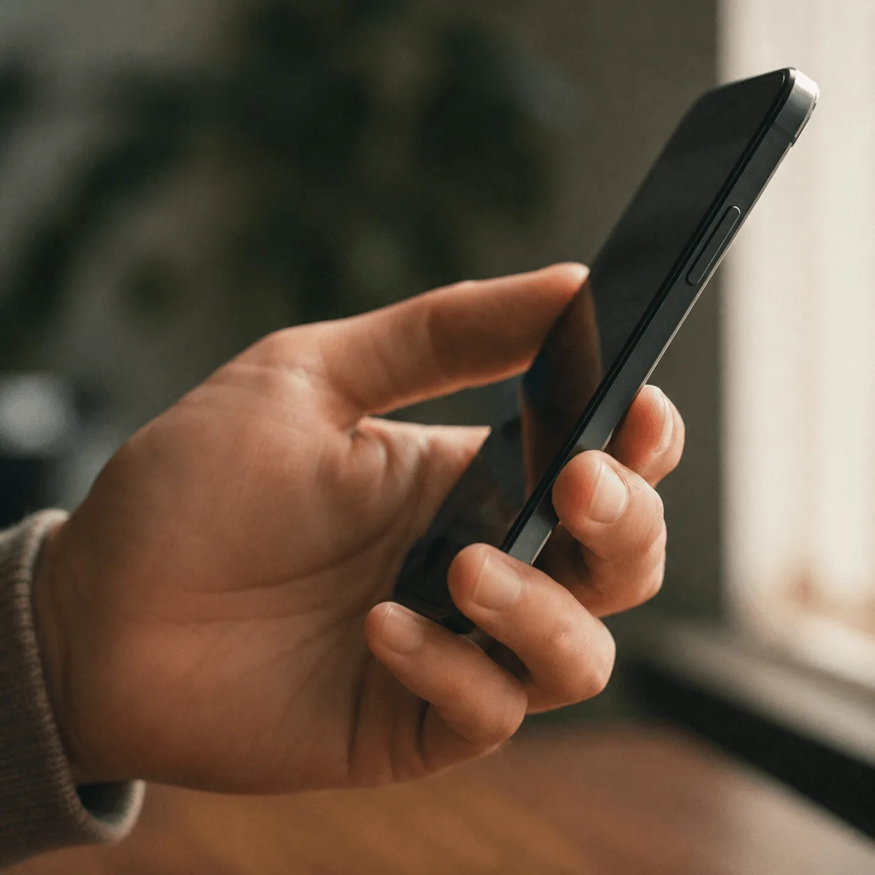 A hand holding a phone with the screen off, about to check a message